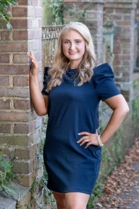 Megan in navy dress smiling by brick wall outdoors