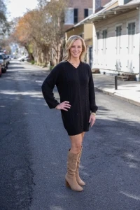 Jeannie smiling in black dress and tan boots posing on city street