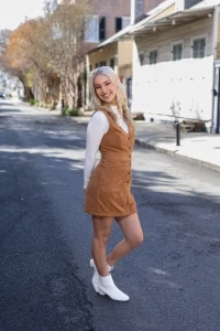 Claire smiling in tan dress and white boots standing on street